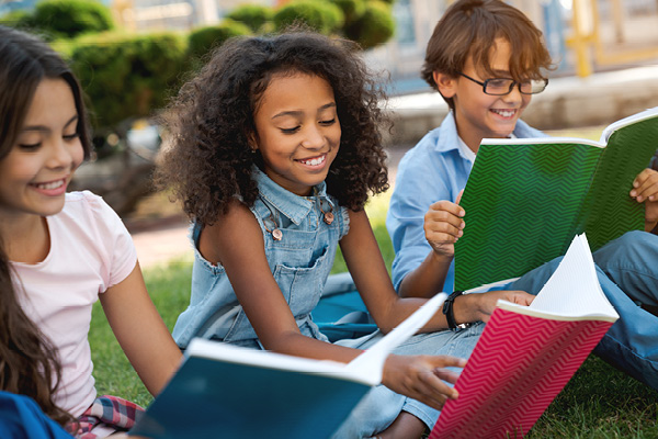 Three children reading books while sitting on a lawn