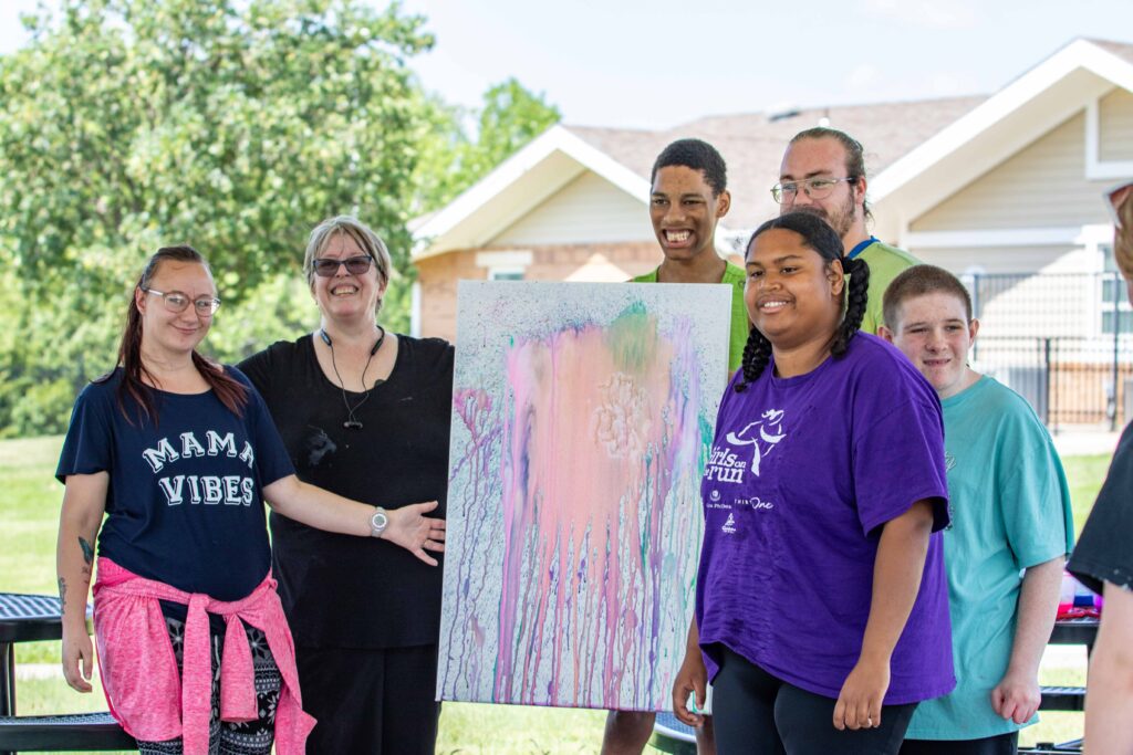 Group of Heartspring staff and students holding up a painting created during Sunday Funday