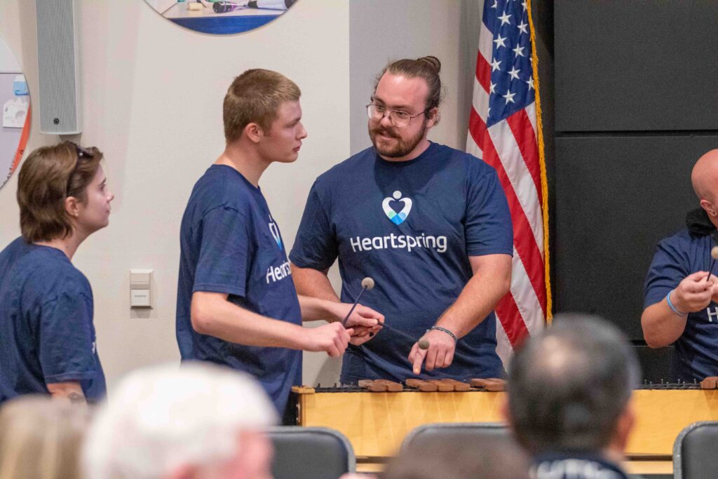 Heartspring direct support professional helping a student play a xylophone during the Family Weekend music program