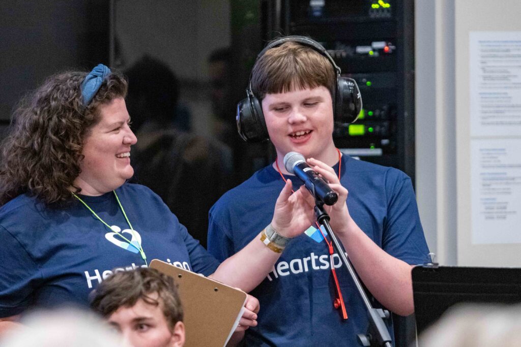 Heartspring School special education teacher and student stand at a microphone during the Family Weekend music program