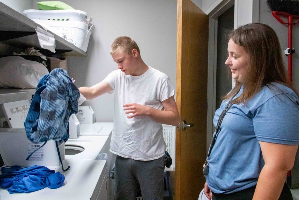 Heartspring direct support professional supervising a student doing his laundry in a residential group home laundry room