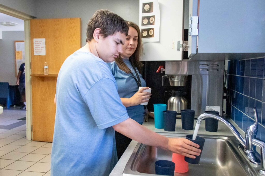 Heartspring direct support professional supervises a student as he independently fills up a cup in a residential group home kitchen