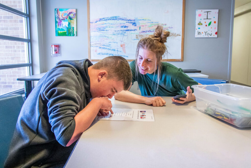 Heartspring direct support professional and student sitting at a table working on reading goals in a group home