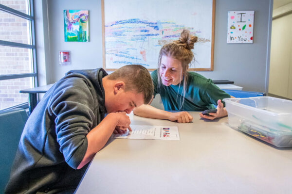 Heartspring direct support professional and student sitting at a table working on reading goals in a group home