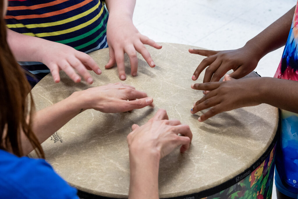 Heartspring music teacher and two CARE Clubs clients playing a large drum together