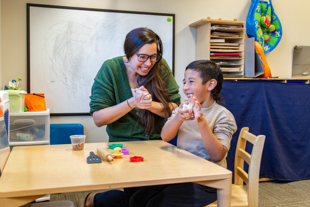 Heartspring occupational therapist working with a client on improving fine motor skills, hand strength, and dexterity by squeezing Play-Doh.
