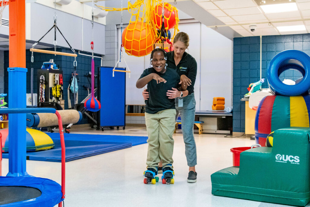 Pediatric physical therapist working with a client on gross motor skills using roller skates