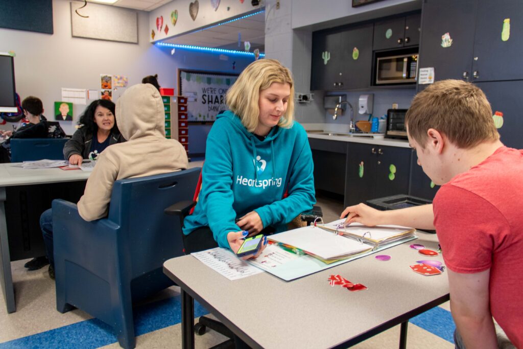 Heartspring direct support professional working with a student on academic goals and tracking progress with an iPod in a classroom setting