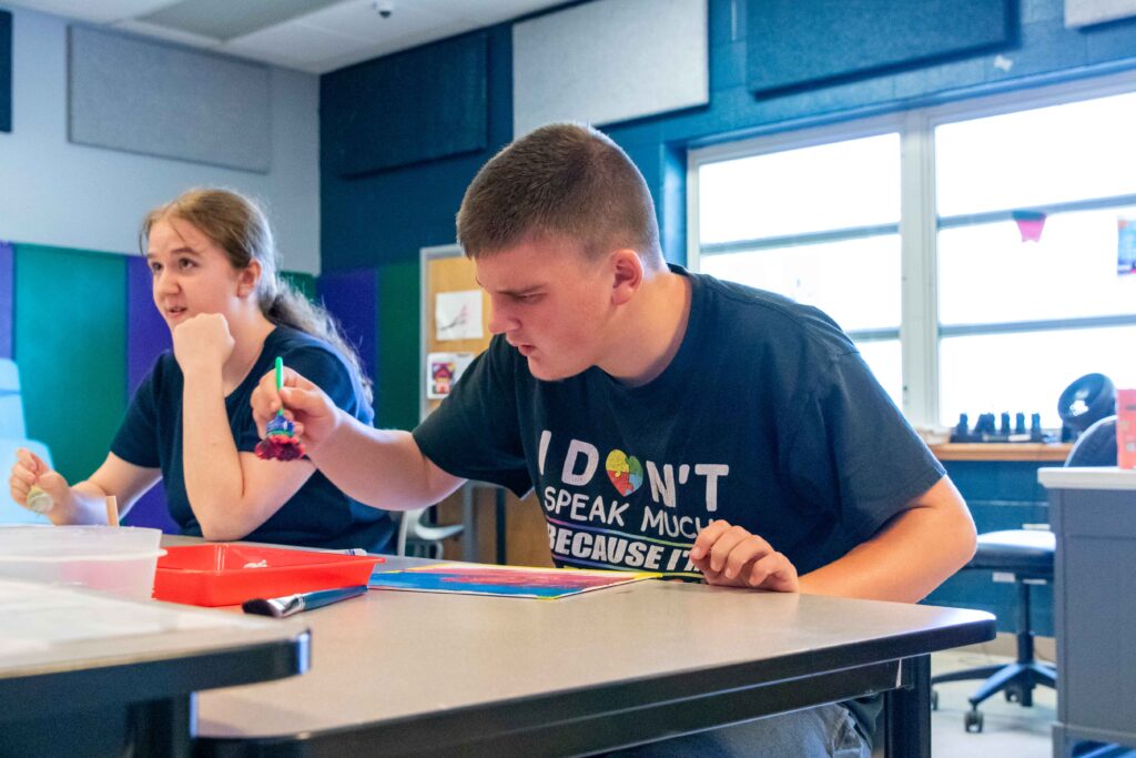 Heartspring student holding a paintbrush while working on an art project and sitting at a desk