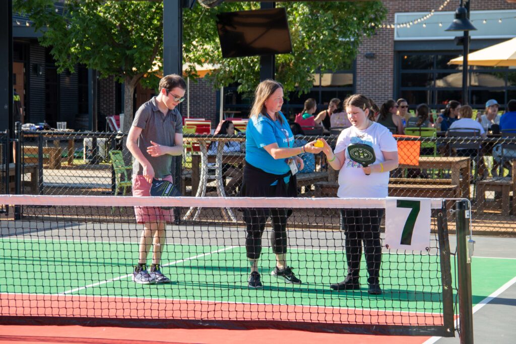Heartspring direct support professional and two students on a pickle ball court at Chicken N Pickle