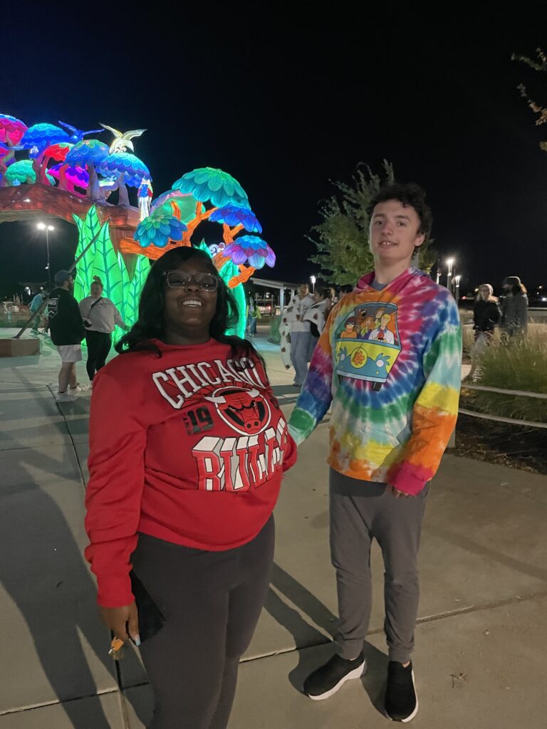 Heartspring direct support professional and student smiling for the camera at a community outing at the Sedgwick County Zoo: Wild Lights