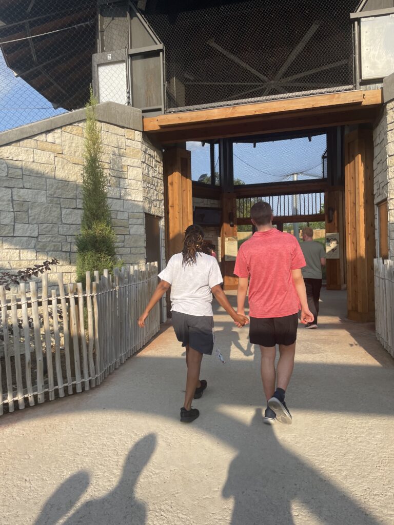 Heartspring direct support professional and student holding hands while walking into an exhibit at the Sedgwick County Zoo