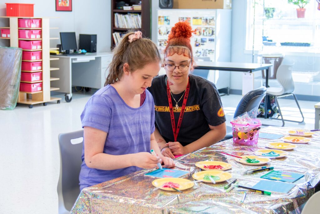 Heartspring direct support professional and student painting and sitting at a table during a Girls Group art activity