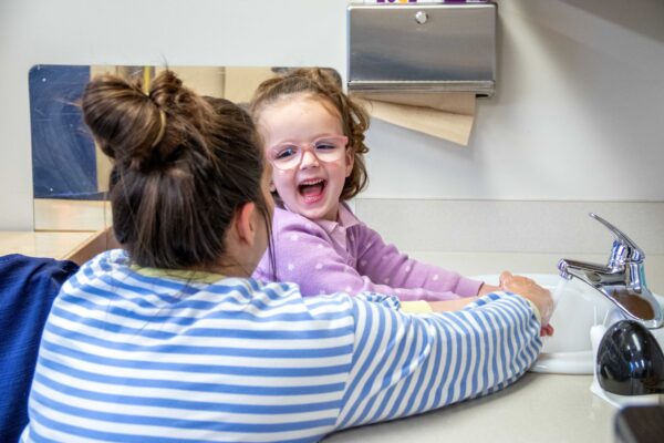Young child smiling and washing her hands with the guidance of her Heartspring occupational therapist in a pediatric occupational therapy early intervention session