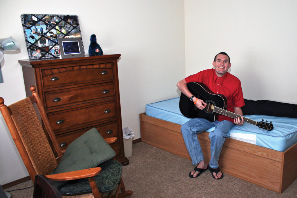 Heartspring student Alex sitting on a bed in his room playing a guitar
