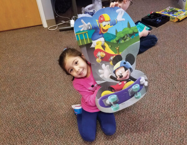 Heartspring pediatric clinic client Angelique holing up a Mickey Mouse and Donald Duck puzzle she assembled
