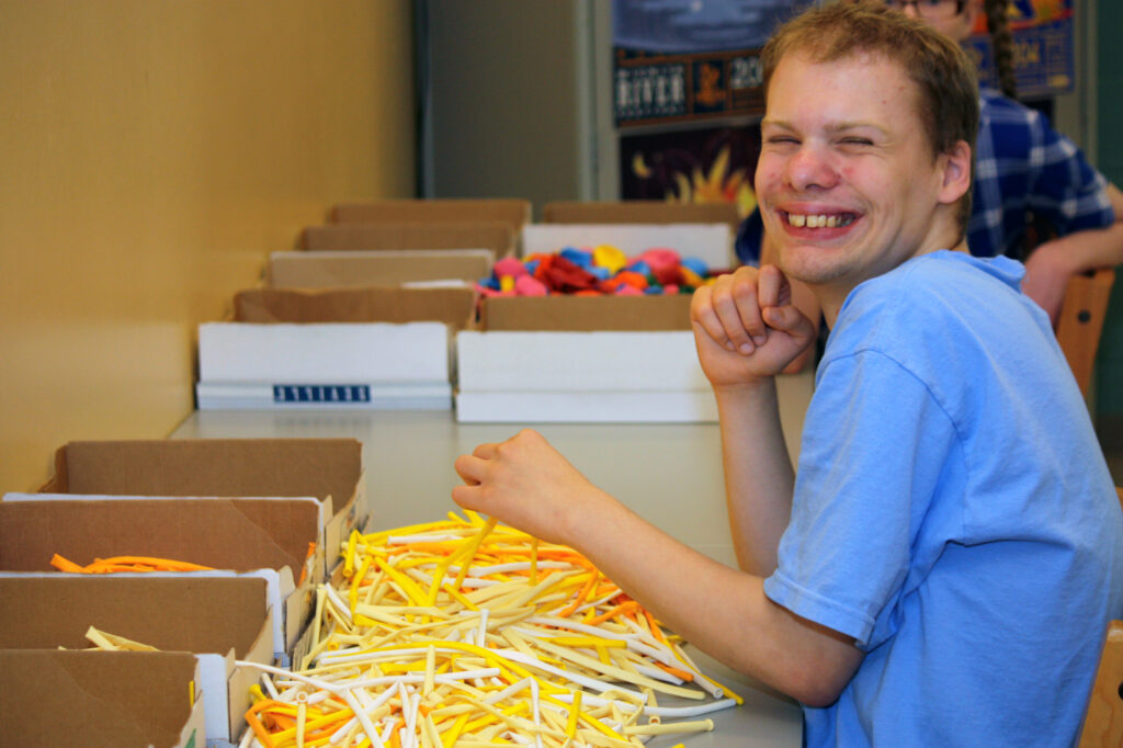 Heartspring student Brady smiling at the camera while working on a sorting task