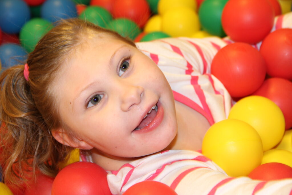 Heartspring pediatric clinic client Braelynn smiling while laying in a ball pit