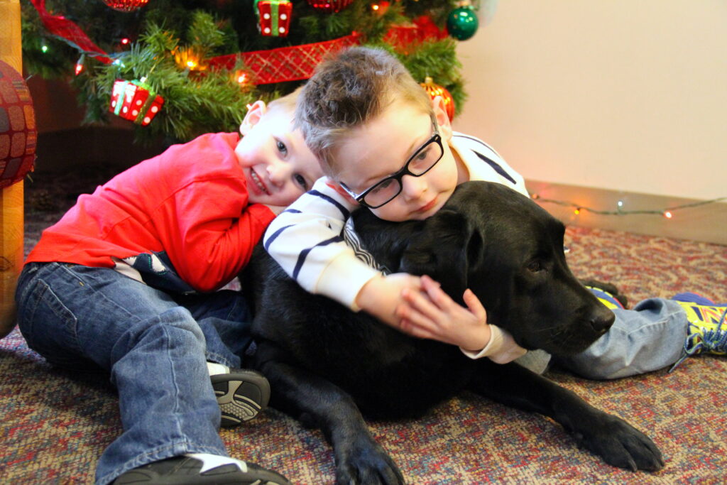 Heartspring pediatric clinic clients Briggan and Cort hug therapy dog Lucy in the clinic lobby