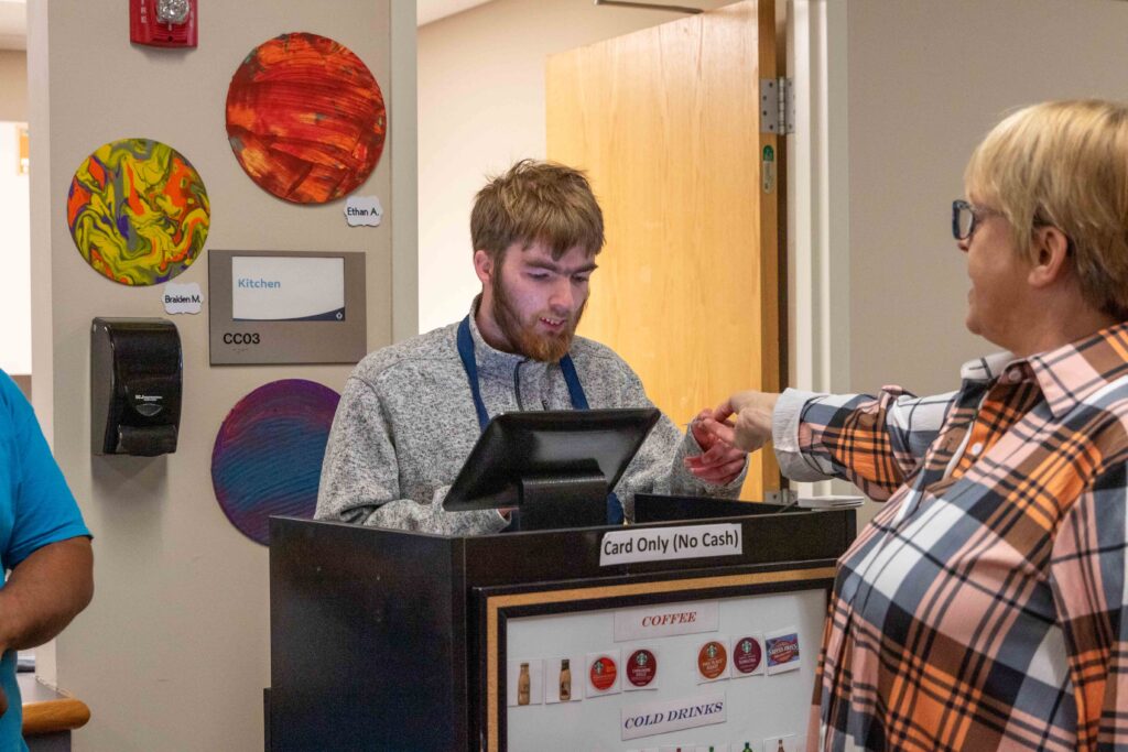 Heartspring student takes payment from a customer for coffee at the Caffeine Connection coffee cart which helps students build vocational and communication skills