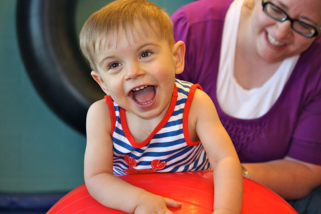 Heartspring occupational therapist helping Colton balance on a ball during a pediatric occupational therapy session