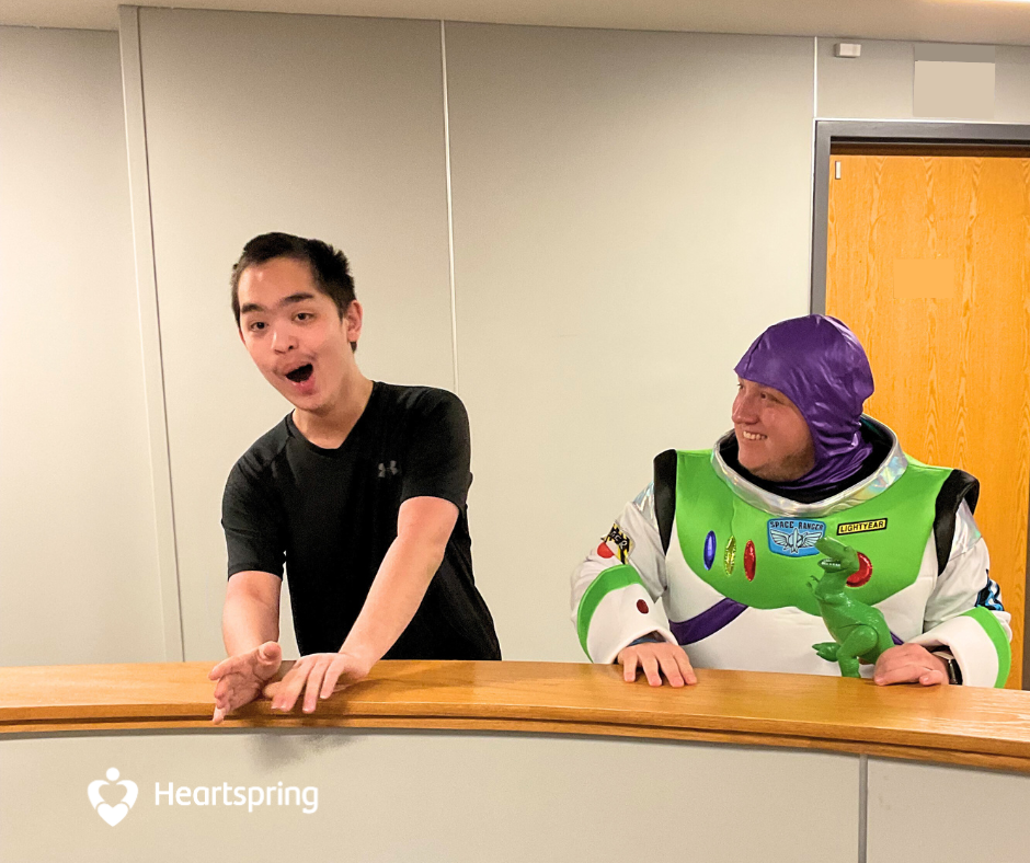 Heartspring special education teacher dressed as Buzz Lightyear and holding a T-Rex, stands next to excited Heartspring Therapeutic Residential School student.