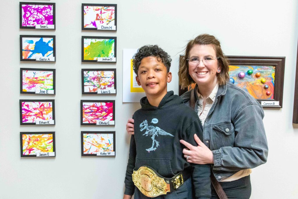 Heartspring student and his mom smiling and posing in front of colorful artwork during the Family Weekend art show