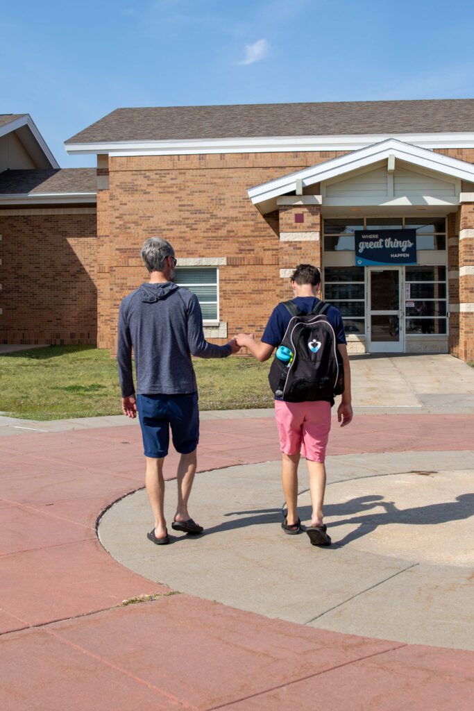 Heartspring student and his dad holding hands and walking away from the camera in the school courtyard during Family Weekend