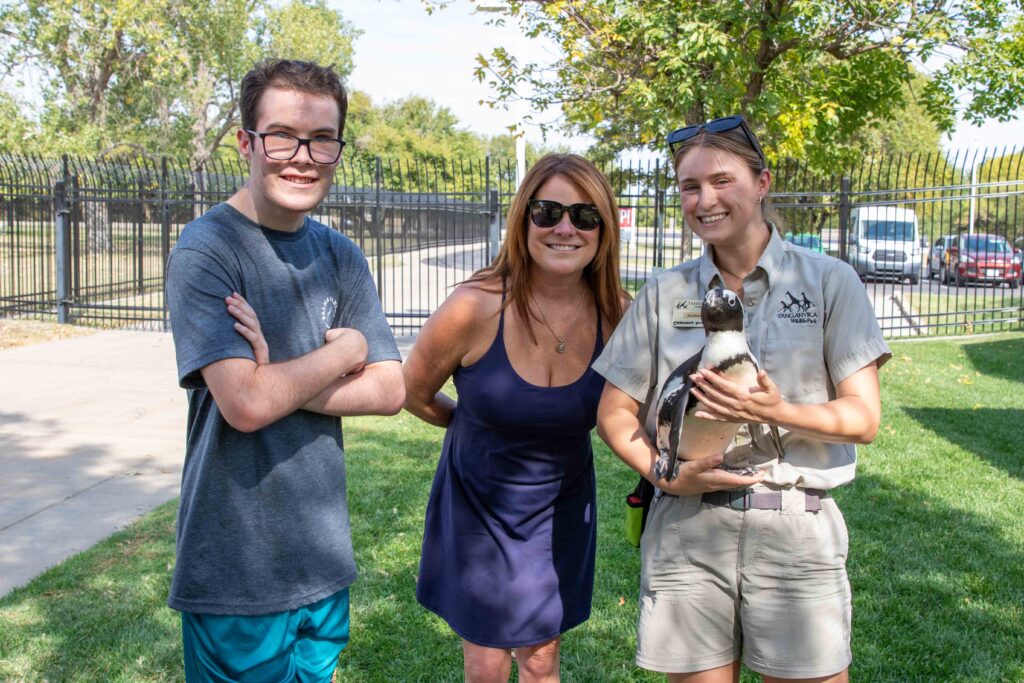 Heartspring student and his mom posing for a photo with a Tanganyika Wildlife Park employee holding a penguin