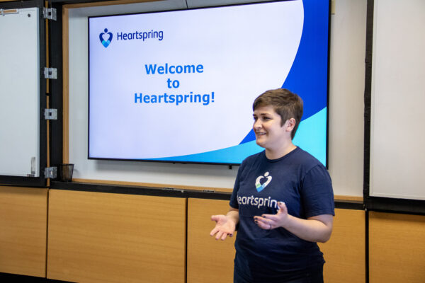 Katie Diaz stands in front of a Heartspring Talent Development PowerPoint presentation slide that says, "Welcome to Heartspring!"