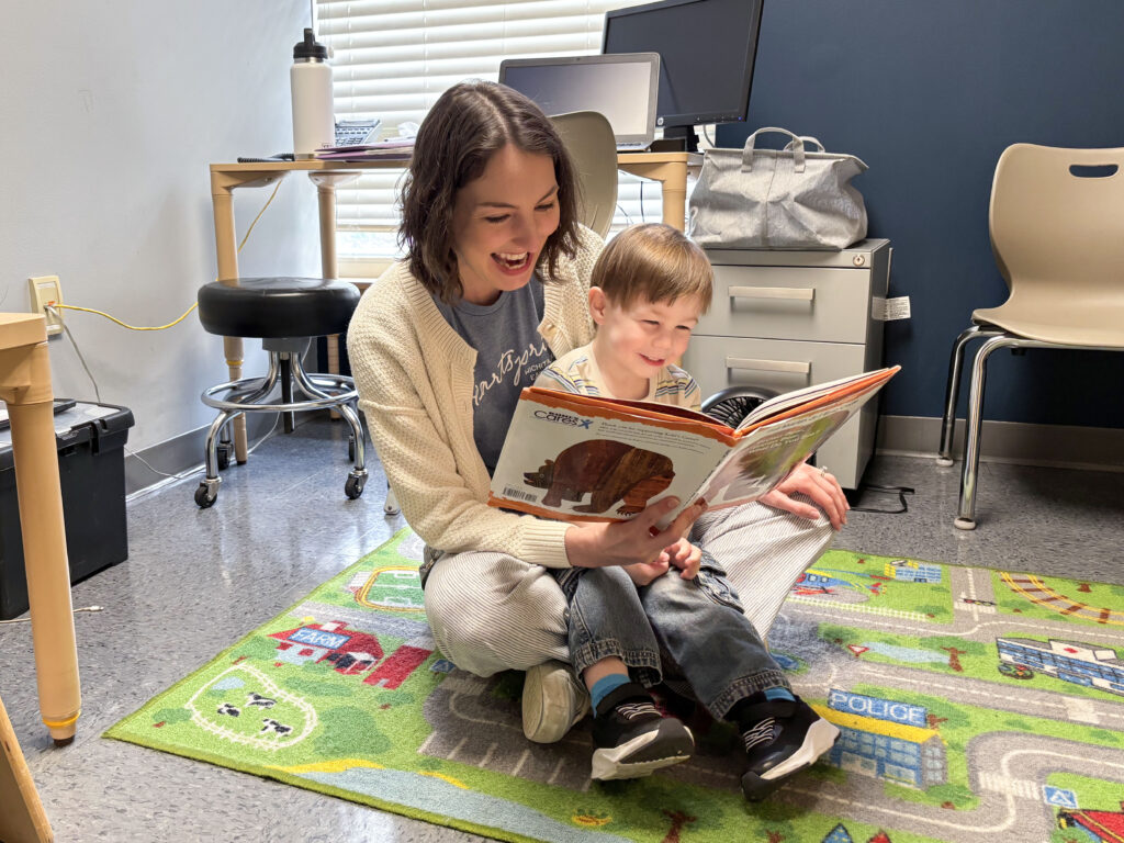Heartspring speech-language therapist and young child sitting in a therapy room reading a book