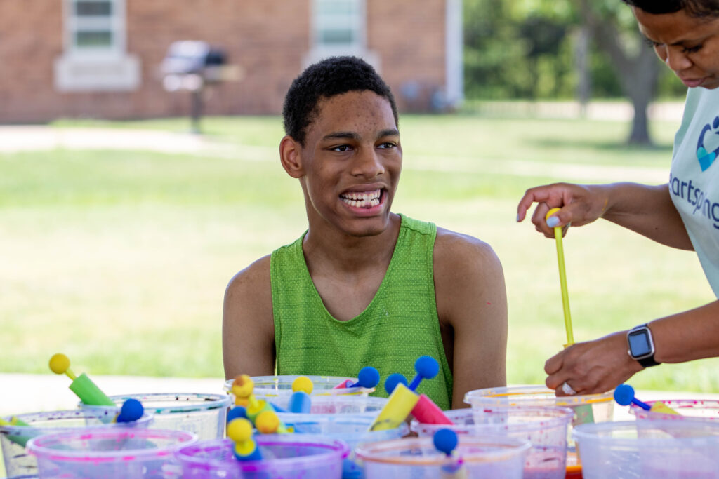 Heartspring student smiling while sitting at a table filled with art supplies for a Sunday Funday activity