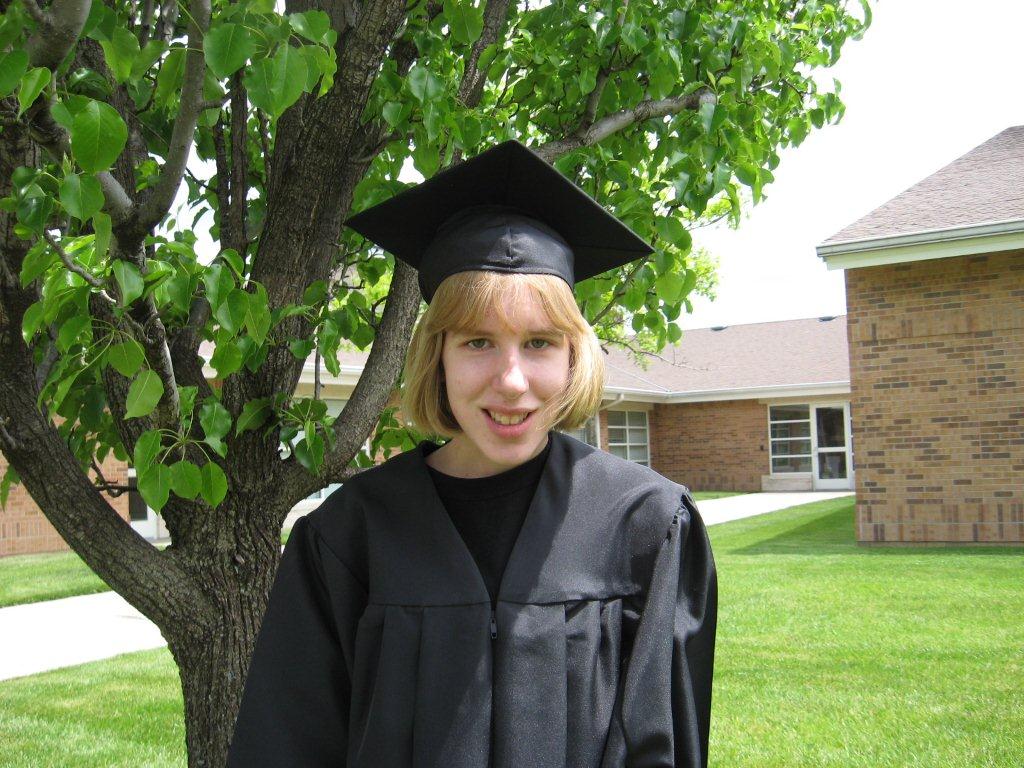 Heartspring student Tessa posing in front of a tree wearing a black graduation cap and gown