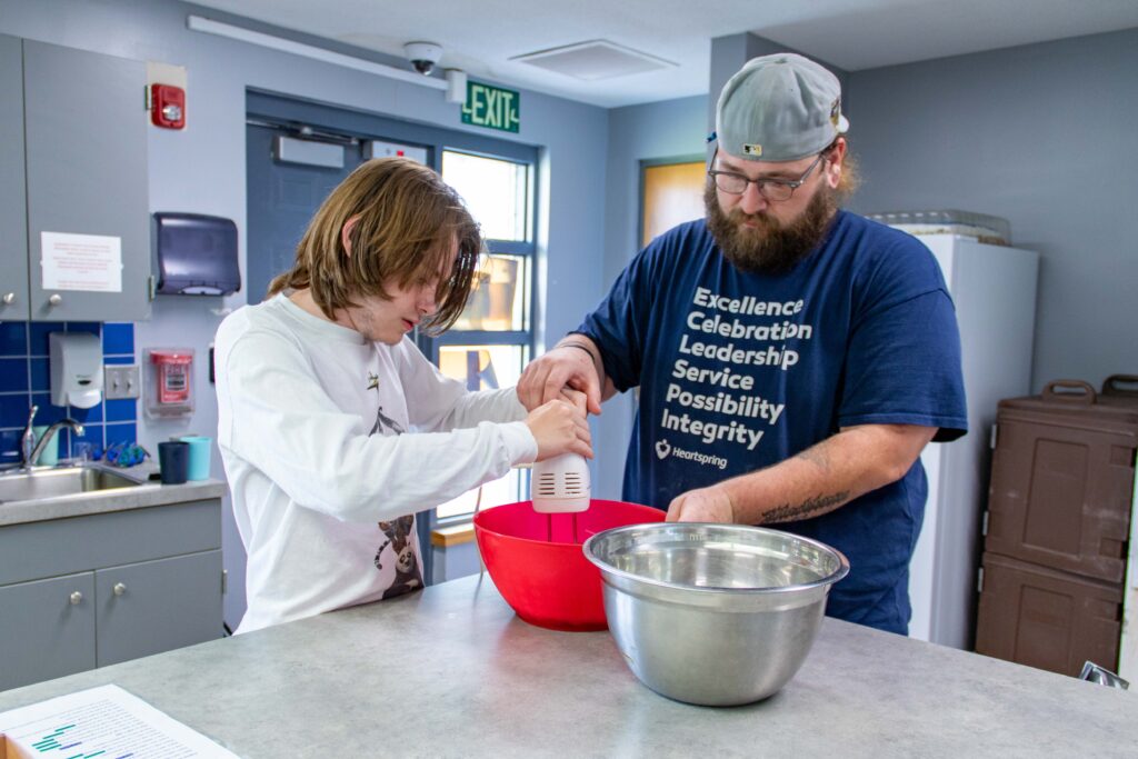 Heartspring student and staff working together mixing cookie dough batter in a residential group home kitchen.