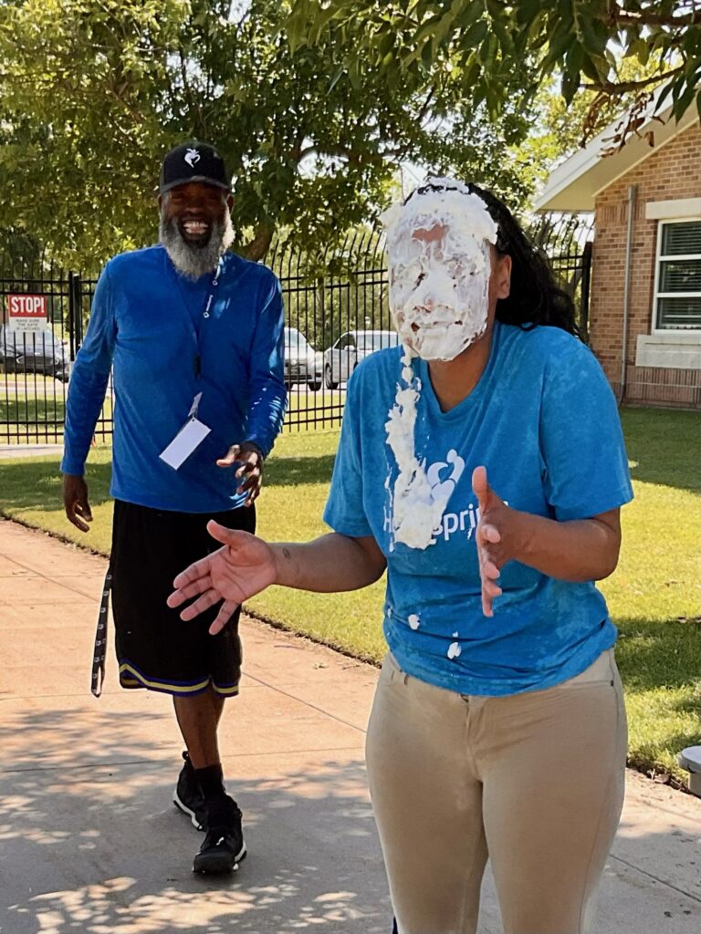 Lysh Dean, G4 supervisor and Values Ambassador, stands with a whip cream "pie" smeared over her face as other staff look on with grins at Heartspring's Therapeutic Residential & Day School Family Field Day.