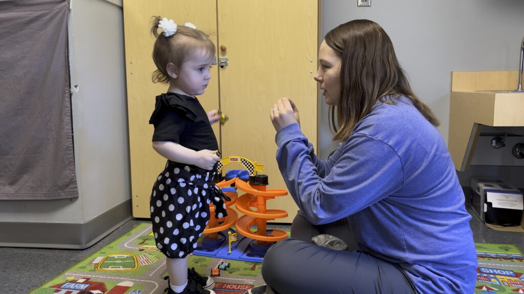 A speech-language pathologist in Heartspring's Outpatient Pediatric Clinic uses the American Sign Language sign for "more" with a young girl in a speech therapy session.