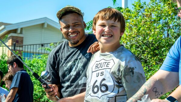 Heartspring Home Assistant Supervisor, Deahvian Manning, stands with a Heartspring Therapeutic Residential & Day School student smiling and fishing in the campus pond.