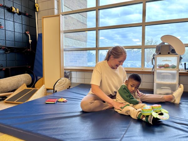 Ryleigh Williams, PT, DPT works with young client on a gymnastics mat in the Heartspring Pediatric Outpatient Clinic physical therapy gym.