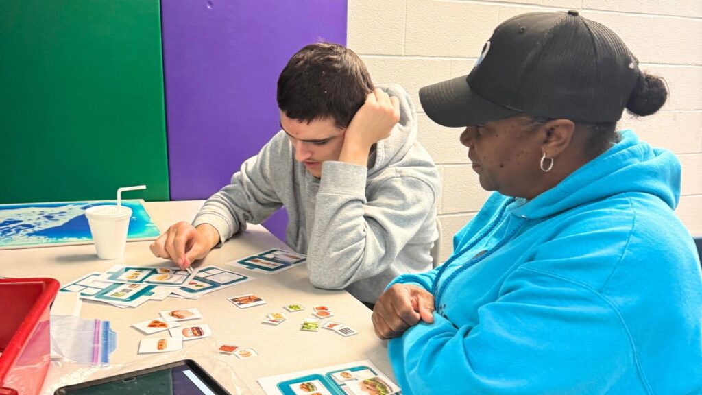 Angela Shack, a lead paraprofessional in the Heartspring Therapeutic Residential & Day School, works with a student at his desk.