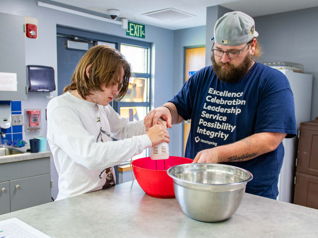 Heartspring student and staff working together mixing cookie dough batter in a residential group home kitchen.