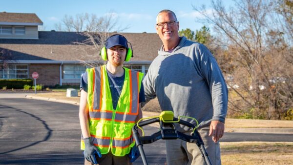 Garret Huebert stands with one of the Heartspring Therapeutic School Students participating in the vocational training program behind a mower.