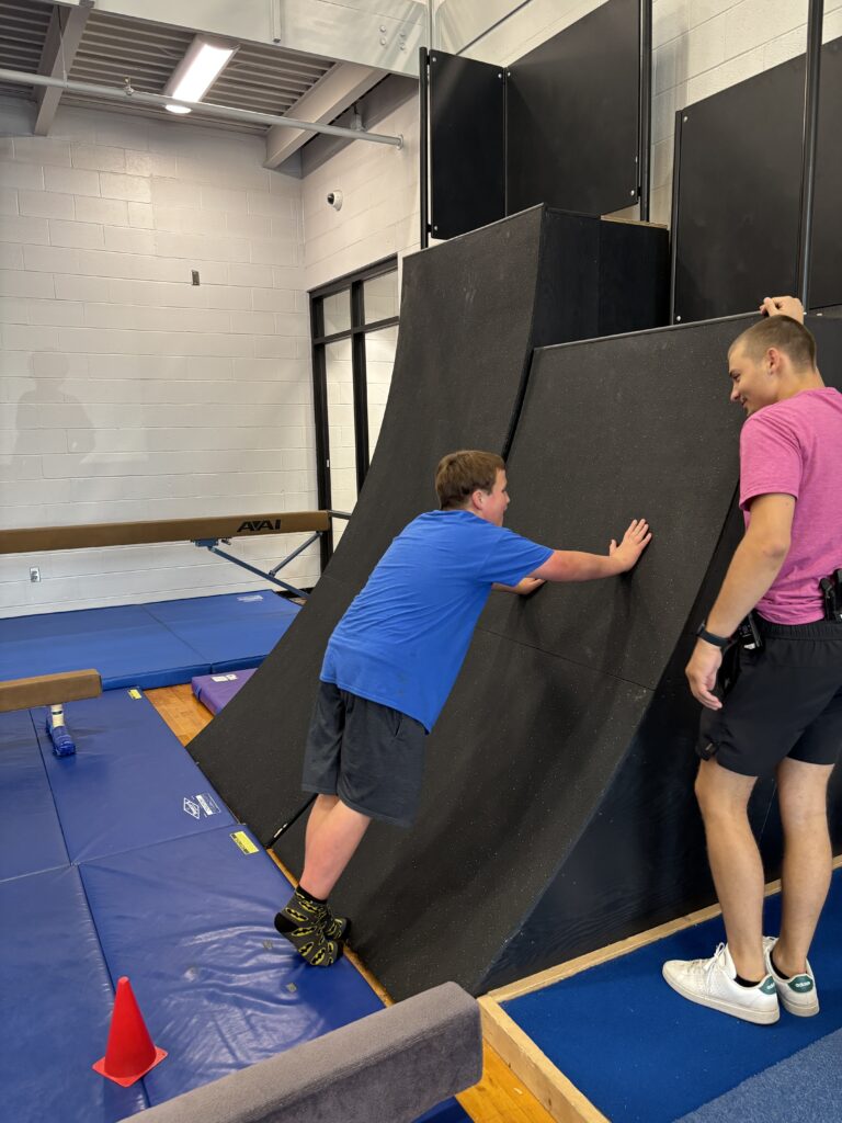 Special education paraprofessional helps a student climb the wall in the YMCA adaptive gymnastics class.