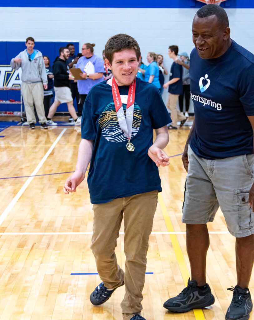 Student and adapted physical education coach smile as he participates in the Kansas Special Olympic Track and Field event.
