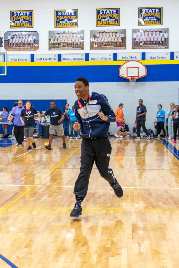 Heartspring student runs in the Kansas Special Olympics Track & Field event as his peers cheer him on in the background.