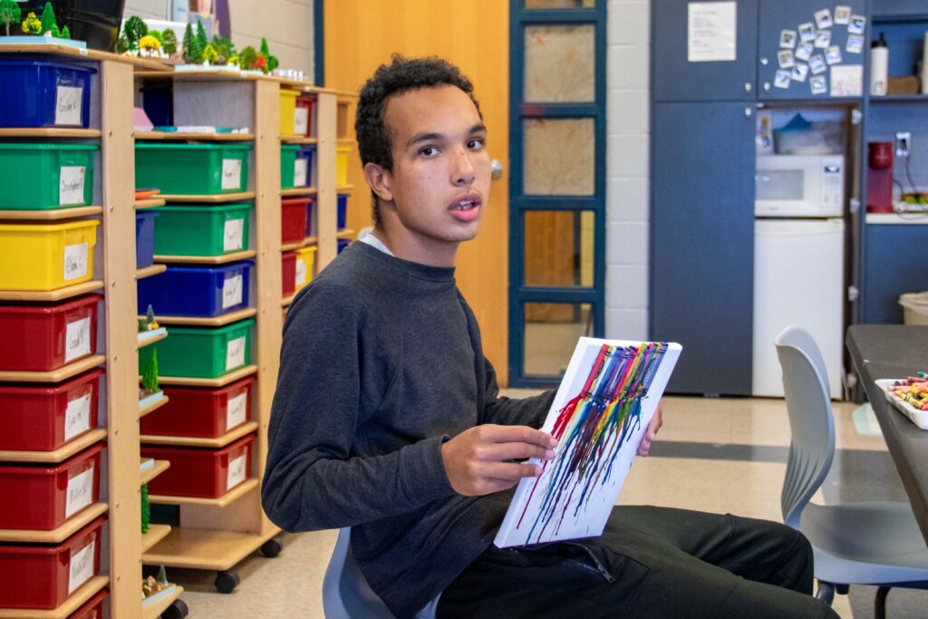 Heartspring student holds up his crayon artwork