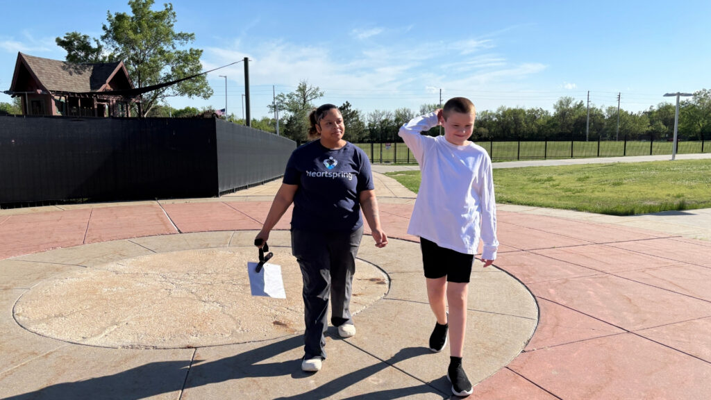 A Residential Home Assistant Supervisor walks with a Heartspring Therapeutic School student on a bright, sunny day around Heartspring's campus.