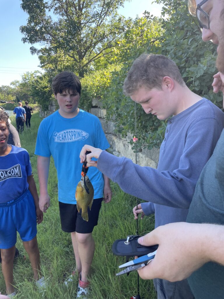 Students in the Heartspring Therapeutic School surround a student who caught a fish in our cmapus catch and release pond.