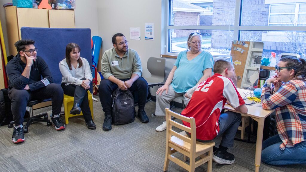 Brandon, a Heartspring Pediatric Outpatient Clinic client, sits with Emily Anderson, an occupational therapist. His grandmother and three WSU students sit to the side of the session to observe.
