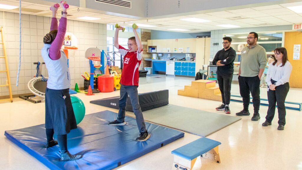 Brandon, a Heartspring Pediatric Outpatient Clinic client, lifts dumbbells with his WSU physical therapist, Leah Fisher.