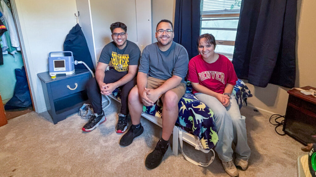 The three WSU engineering students responsible for creating Brandon's Murphy bed solution sit on the bed side-by-side.